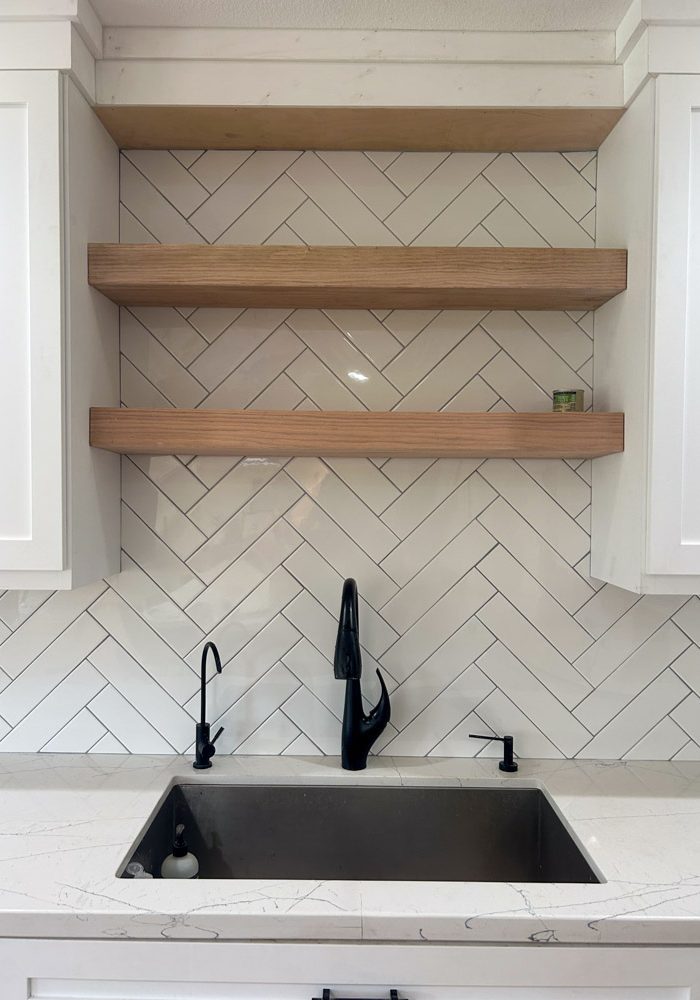 Chevron tile backsplash installed in the kitchen with wall mounted wood shelves in between cabinets