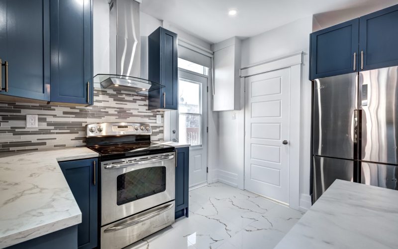 A kitchen with blue cabinets, marble countertops, tile flooring, and tile backsplash